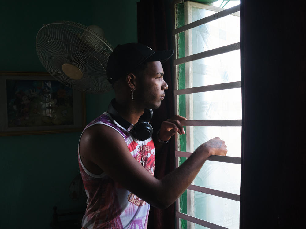 Gabriel Berrio Fabré, 18, looks out the window of his room in Los Pocitos, Havana. He is a visual artist, and like most of his friends, he wants to leave Cuba once he finishes his studies.