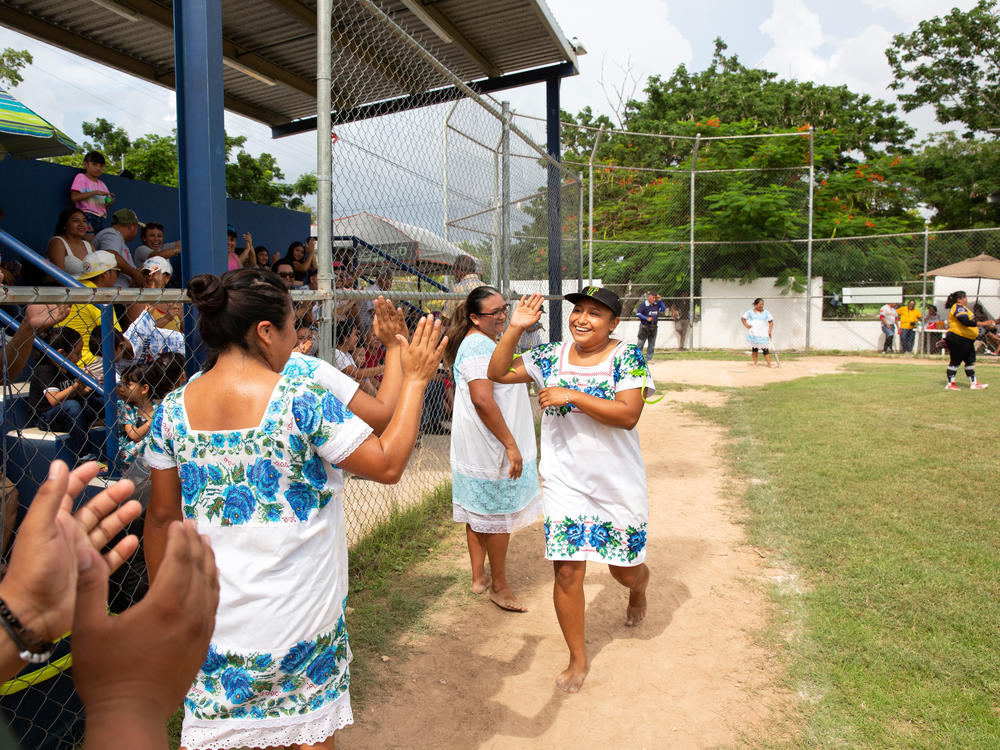 Sitlali Yovana Poot Dzib, 20 (left), captain of The Amazonas of Yaxunah, high fives her teammates after a home run in a game played on Sept. 10. The indigenous women on the team live in the small Maya community of Yaxunah in Mexico's Yucatán Peninsula. They wear traditional Maya garb when they play — and eschew shoes.