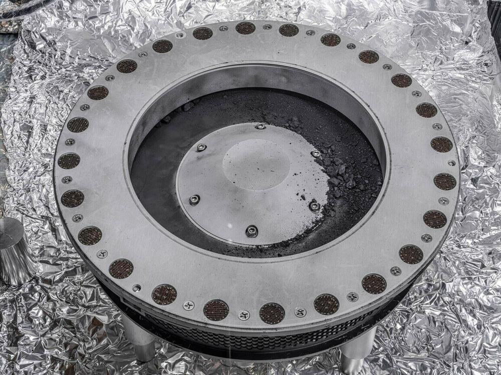 Small rocks and dust from an asteroid, outside a round sample collection device in a NASA lab.