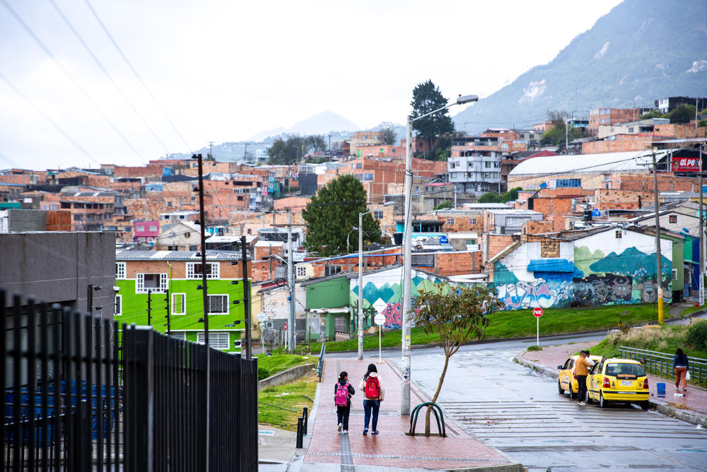 Infante and daughter Brigitte walk home from school with the Andes mountains as a backdrop. Infante says she doesn't mind being the family caregiver, but the work is relentless and stressful and leaves her with no time to hold a paid job.