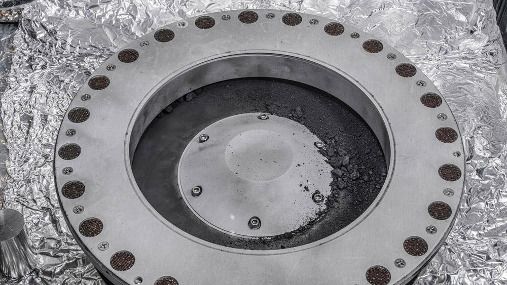 Small rocks and dust from an asteroid, outside a round sample collection device in a NASA lab.