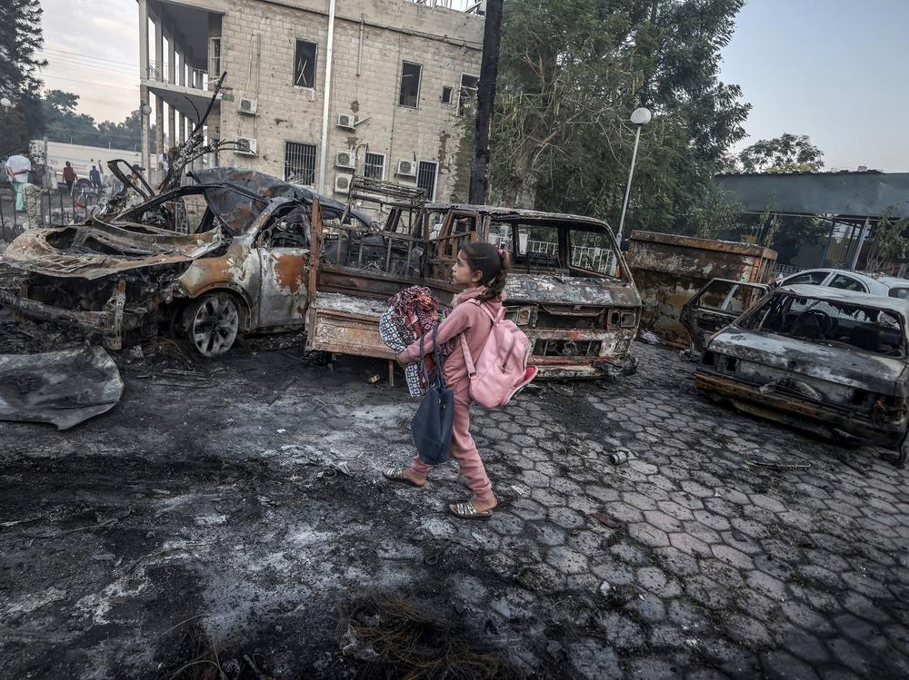 A girl tries to collect usable belongings amid the wreckage of vehicles after the explosion at Al Ahli Arab Hospital in Gaza.