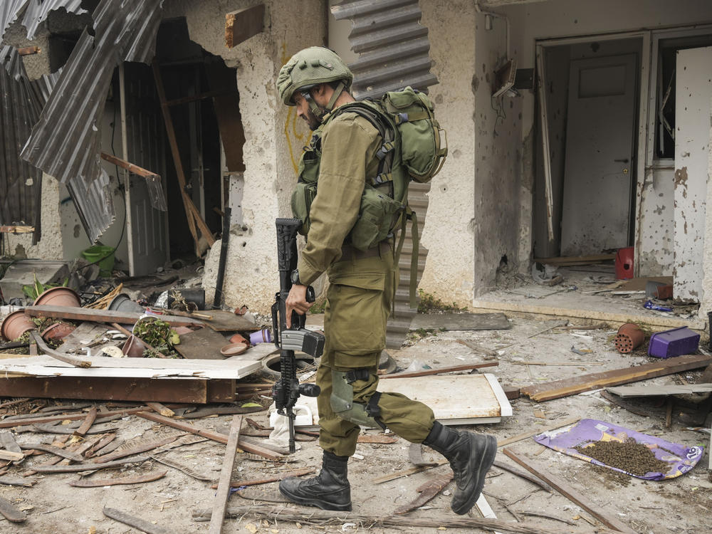 An Israeli soldier walks past a house damaged during the Hamas attack in Kibbutz Kfar Azza, Israel, on Friday. The Kibbutz was attacked on Oct. 7.