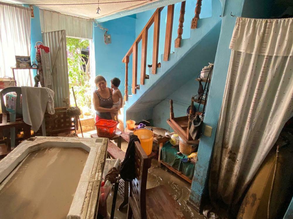 Antonia Hernández carries her 2-year-old grandson through her mud-covered house.