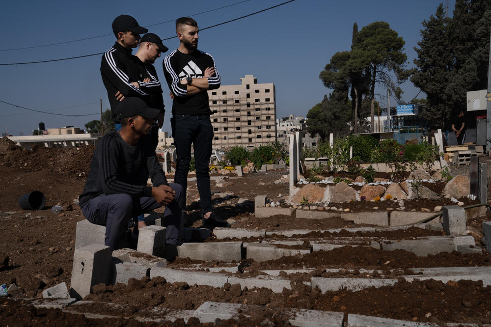 Young men stand in front of recently dug graves of people killed by Israeli forces in Jenin. More than 100 Palestinians have been killed in the West Bank in the three weeks since the war began.