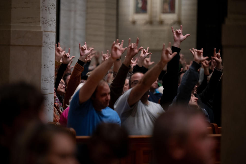 Community memebers sign 'I love you' as Kevin Bohlin, a member of the deaf community, delivers remarks in American Sign Language in the Basilica of Saints Peter and Paul in Lewiston, Maine.