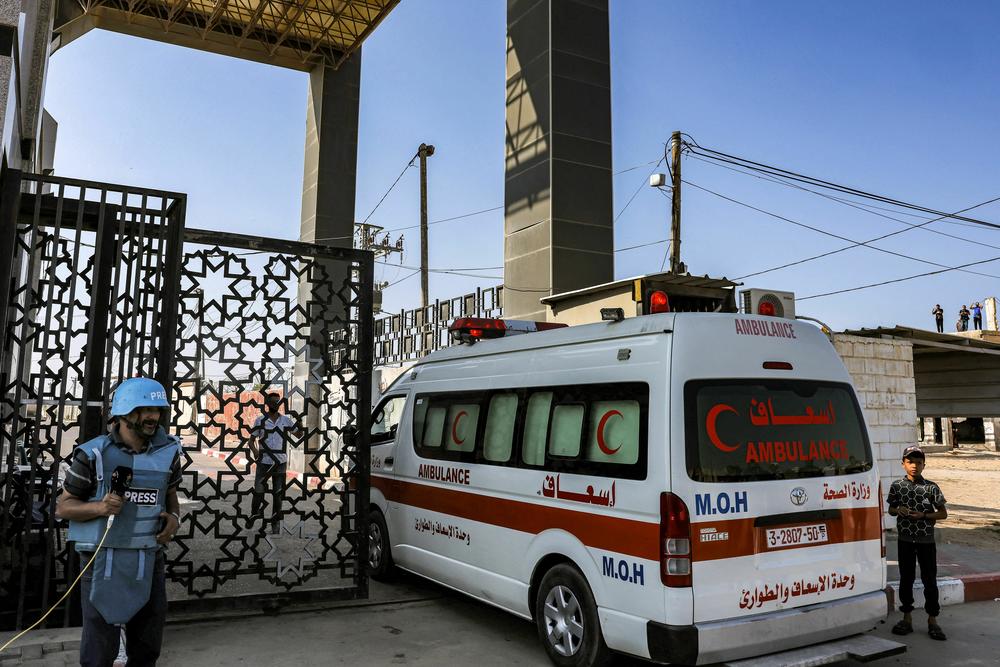 A journalist stands by as Palestinian health ministry ambulances cross the gate to enter the Rafah border crossing in the southern Gaza Strip before crossing into Egypt.