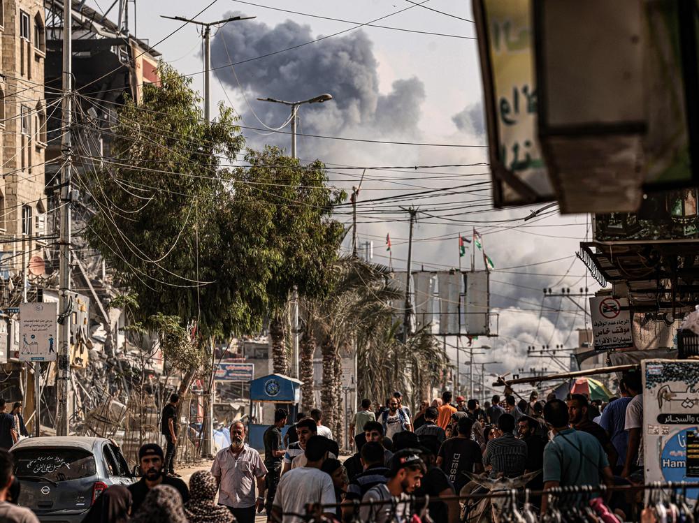 People walk along a street as a plume of smoke rises in the background during an Israeli strike on the Bureij refugee camp in the Gaza Strip on Thursday, as battles between Israel and the Palestinian Hamas movement continue.