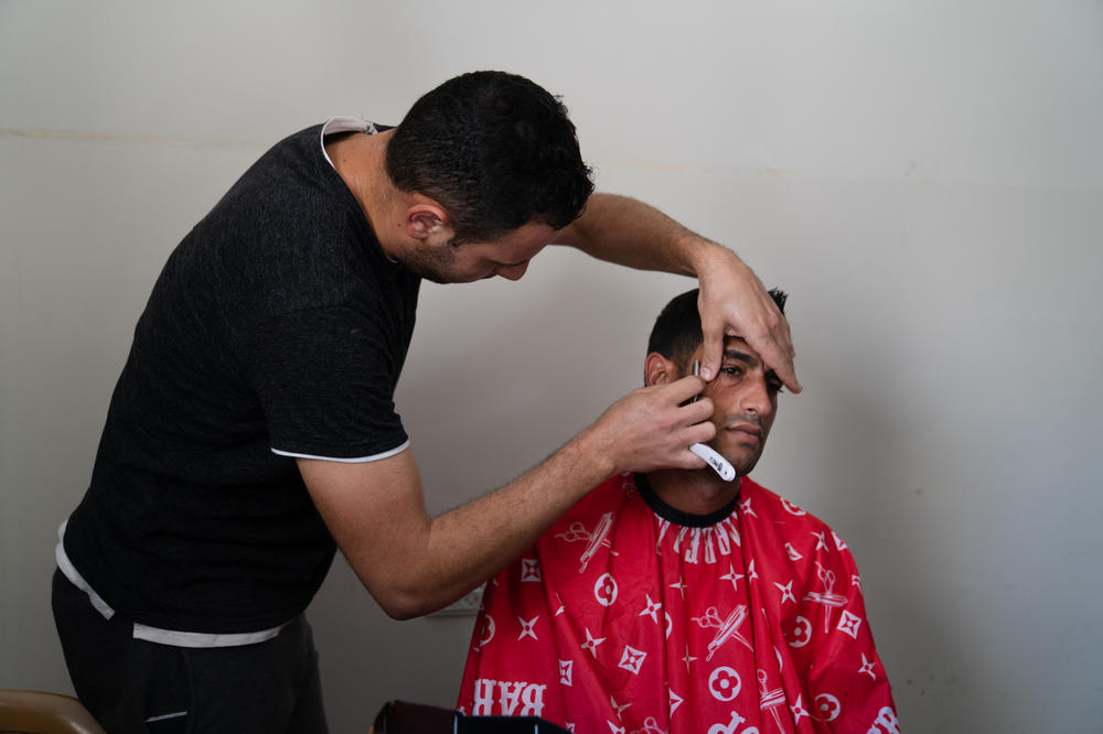 Ibrahim Alfarany gets a shave from a barber at the university. Both are displaced from their homes. With the large number of workers staying at the shelter, they have to sign up on a wait list to get a haircut and shave.