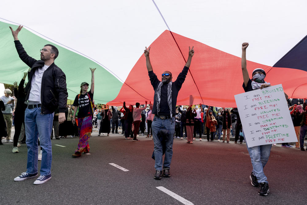 Protesters walk underneath a large Palestinian flag. Protesters are pushing for a cease-fire in Gaza.