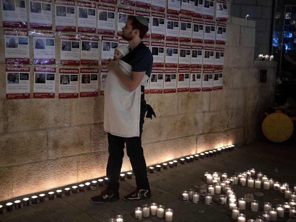 A man holds his baby Sunday in Jerusalem as he looks at posters of the men, women and children held hostage by Hamas in the Gaza Strip, during a vigil marking 30 days since the Oct. 7 Hamas attack that started the fighting.