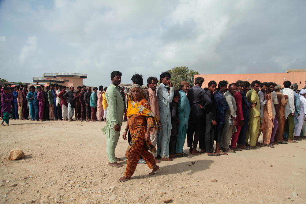 A woman walks past lines of men waiting for donations of food from a charity in the fishing village of Keti Bandar, at the mouth of the Indus River Delta in southern Pakistan. Poverty here is still widespread although fishermen say their lives have been improving since mangrove reforestation efforts began here in earnest a few years ago.