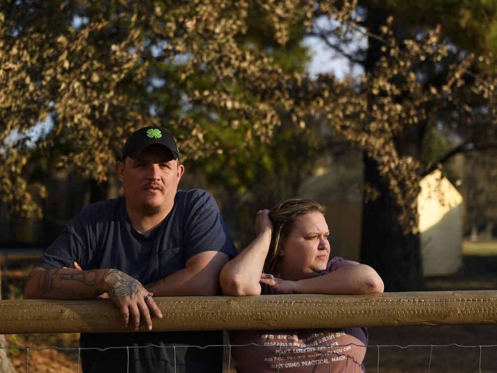 Army veteran Ray Queen stands with his wife, Rebecca Queen, outside their home in Bartlesville, Okla. An NPR investigation has found that thousands of U.S. military service members and veterans, including the Queen family, are at risk of losing their homes through no fault of their own.