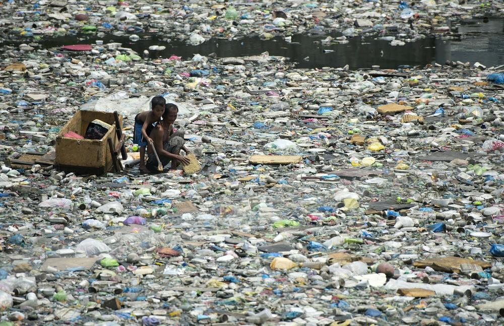 A father and son on a makeshift boat in the Philippines collect plastic bottles to sell in Manila.