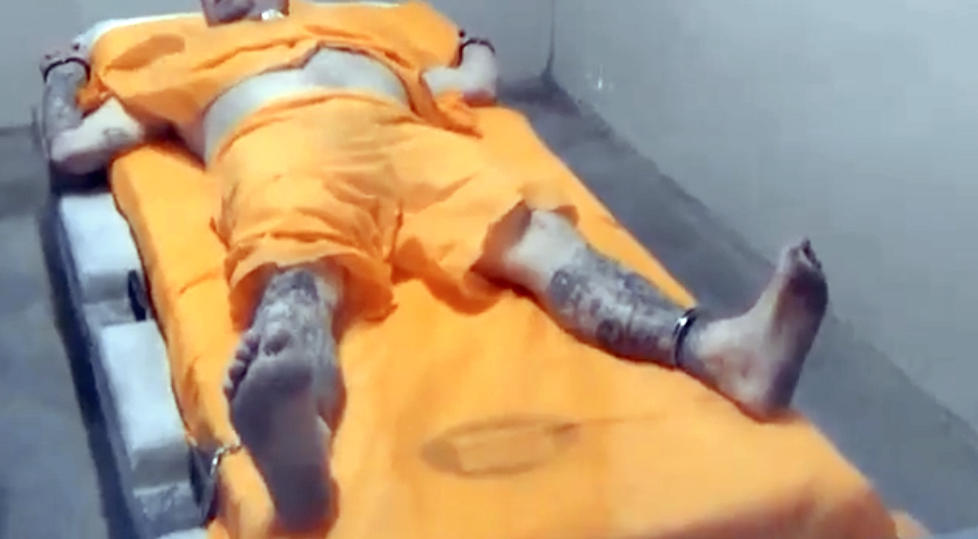 Officers at Thomson prison hold a man in a four-point restraint, with wrists and ankles secured to restrict movement.