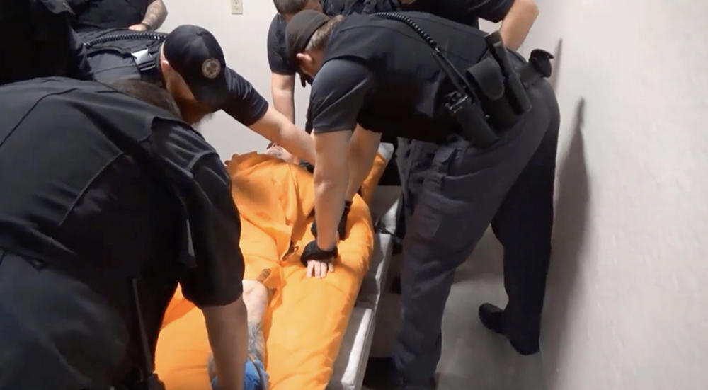 A man is held down by a group of officers at Thomson prison as they try to place him in a four-point restraint.