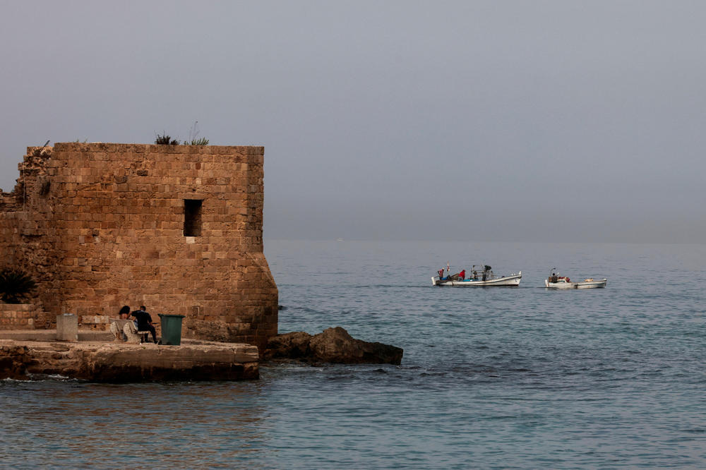 A couple sits as fishermen are seen in their boats in the port city of Tyre, Lebanon, on Oct. 27.