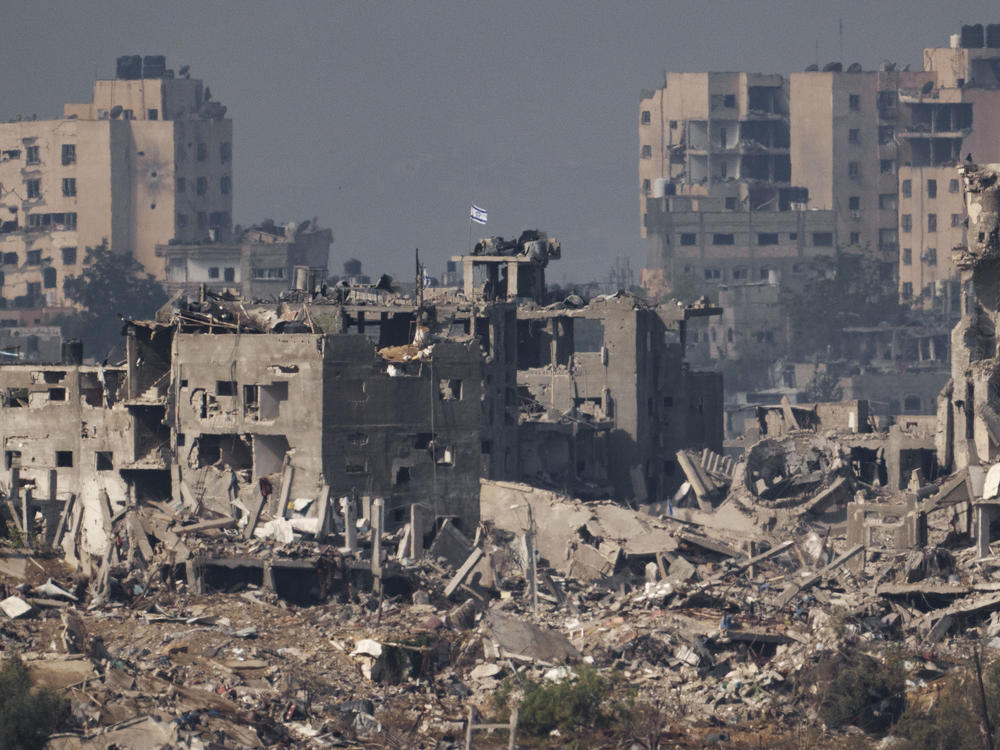 An Israeli flag stands atop a destroyed building in the Gaza Strip, as seen from southern Israel, on Wednesday.