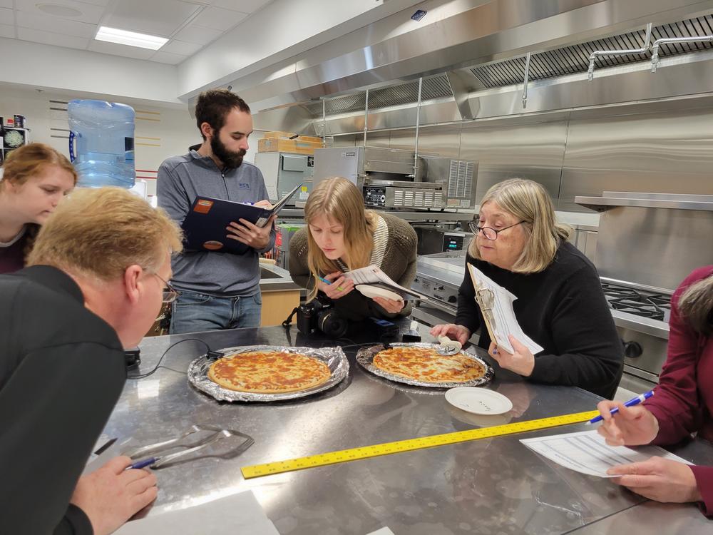 Cheese testers lean in to inspect pizzas at the University of Wisconsin's Center for Dairy Research in Madison.