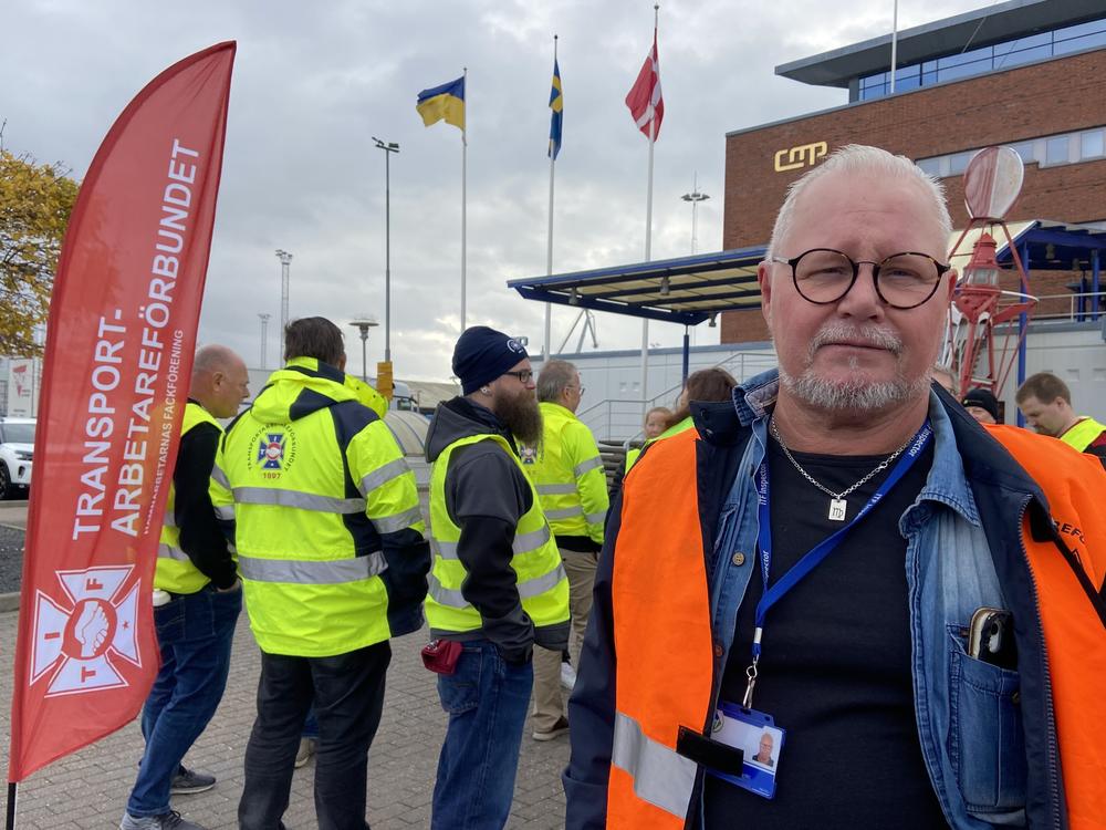 Goran Larsson, a cargo ship inspector, poses next to the Transport Workers' Union flag at the Malmo port on Nov. 7. Dockworkers are refusing to load or unload Teslas at this port and all others across the country.
