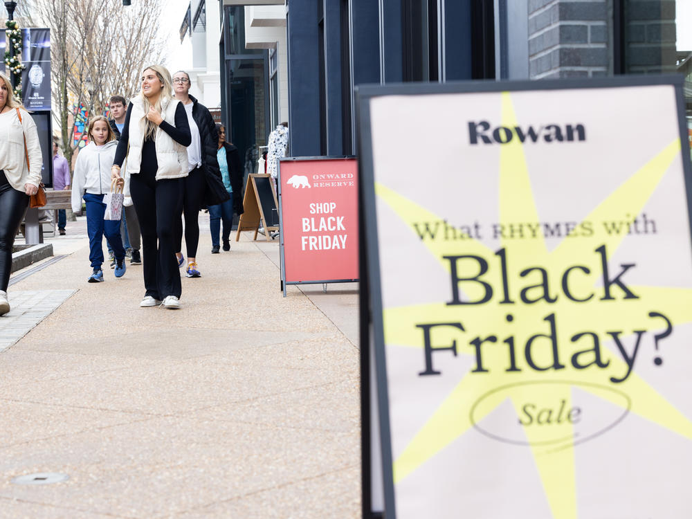 Shoppers walk past sale signs at the Avalon shopping center in Alpharetta, Ga., during Black Friday in 2022.