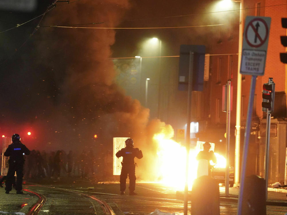 A car burns as Irish policemen stand at the scene of an attack in Dublin city centre, Thursday Nov. 23, 2023.