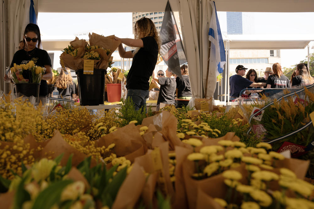 Volunteers sell yellow flowers to benefit hostage families in the square in front of the Tel Aviv museum.