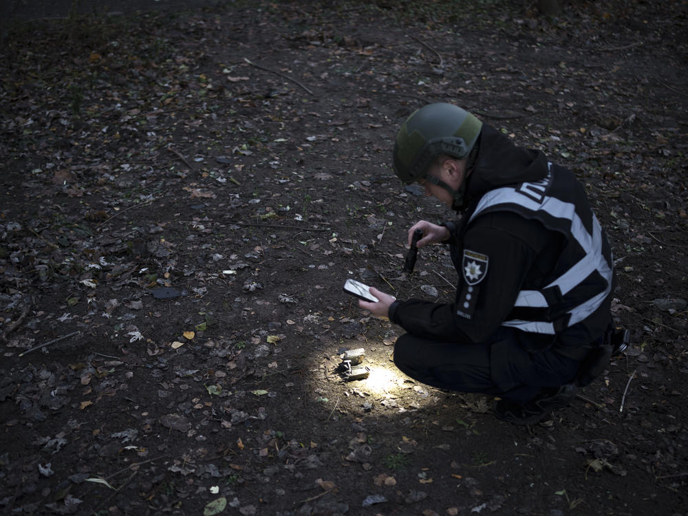 A Ukrainian police officer uses a flashlight to search for drone debris near the site of an explosion following a Russian drone attack in Kyiv, Ukraine, on Saturday, Nov. 25, 2023, its most intense on the Ukrainian capital since the beginning of its invasion, military officials said.
