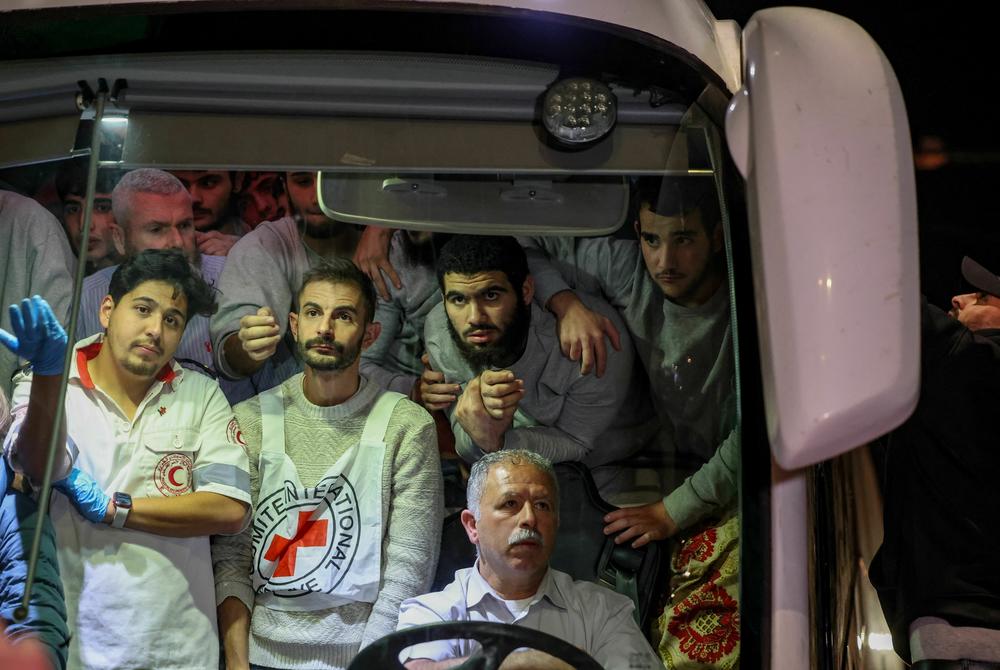 A man climbs on the side as Red Cross staff and Palestinians prisoners released from Israeli jails in exchange for hostages released by Hamas from the Gaza Strip, stand inside a bus as they are welcomed by crowds in Ramallah in the occupied West Bank early on Nov. 26, 2023.