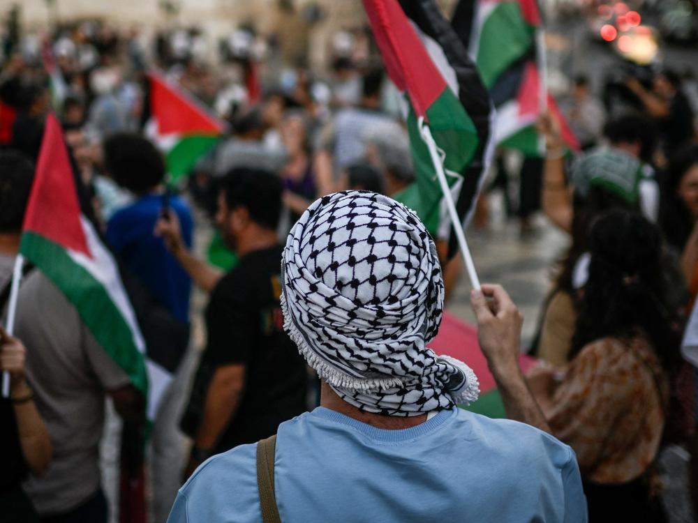 A protestor wearing a keffiyeh waves a Palestinian flag during a rally in support of Palestinians in Lisbon in October.
