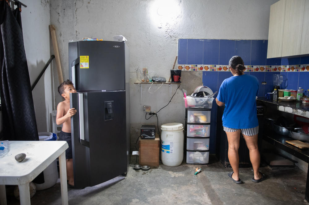 July prepares breakfast for her 6-year-old son, Samuel. She and her husband spend a significant amount of their monthly income to purchase water for drinking. The white container by her side holds water for washing dishes.
