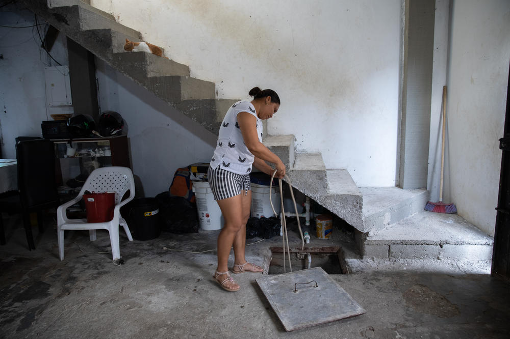 July Merino shows how she retrieves water from the <em>alberca</em> in her home. The concrete cistern can store about two weeks of water that her family uses to do laundry, wash dishes and flush the toilet.