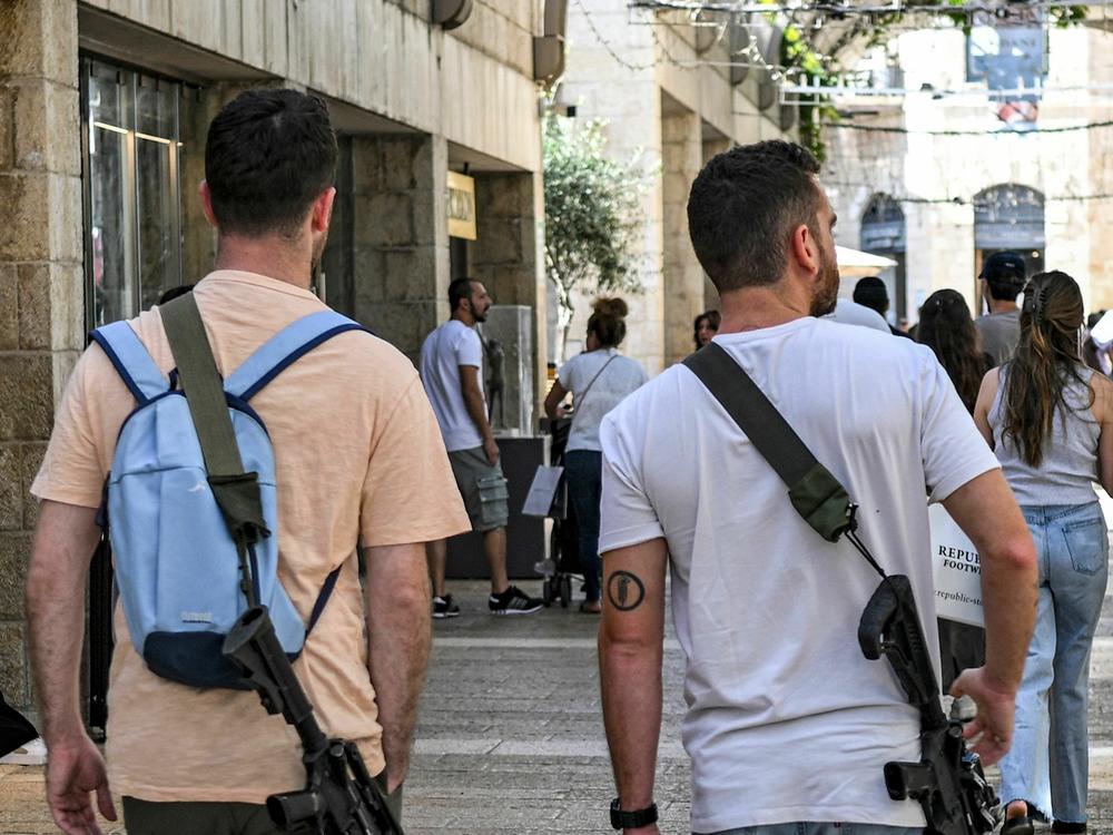 Israeli men, armed with U.S.-made M16 automatic assault rifles, walk in a shopping center in Jerusalem on Oct. 25, amid the ongoing battles in the Gaza Strip between Israel and Hamas.