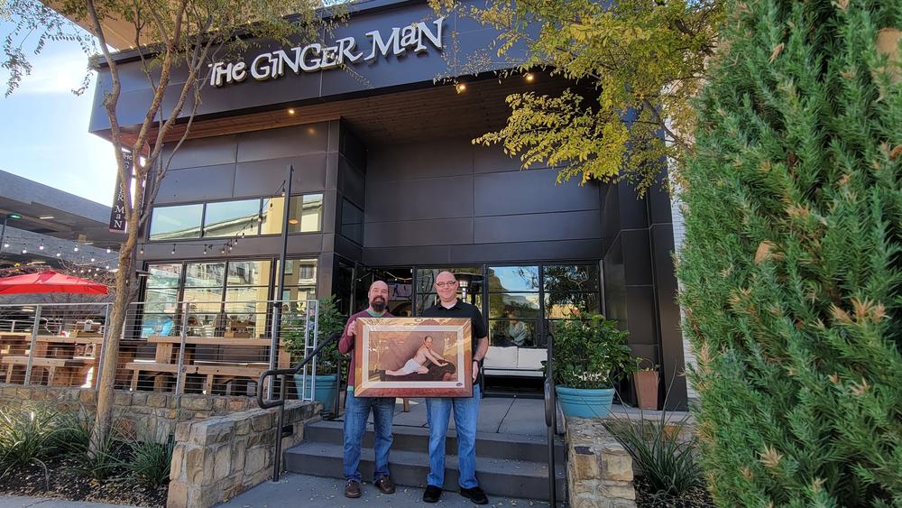 Mark McKee (L) and Jason Talkington (R) hold McKee's framed poster of <em>Seinfeld</em>'s George Costanza outside The Ginger Man bar in Irving, Tx., which hosts an annual Festivus event.