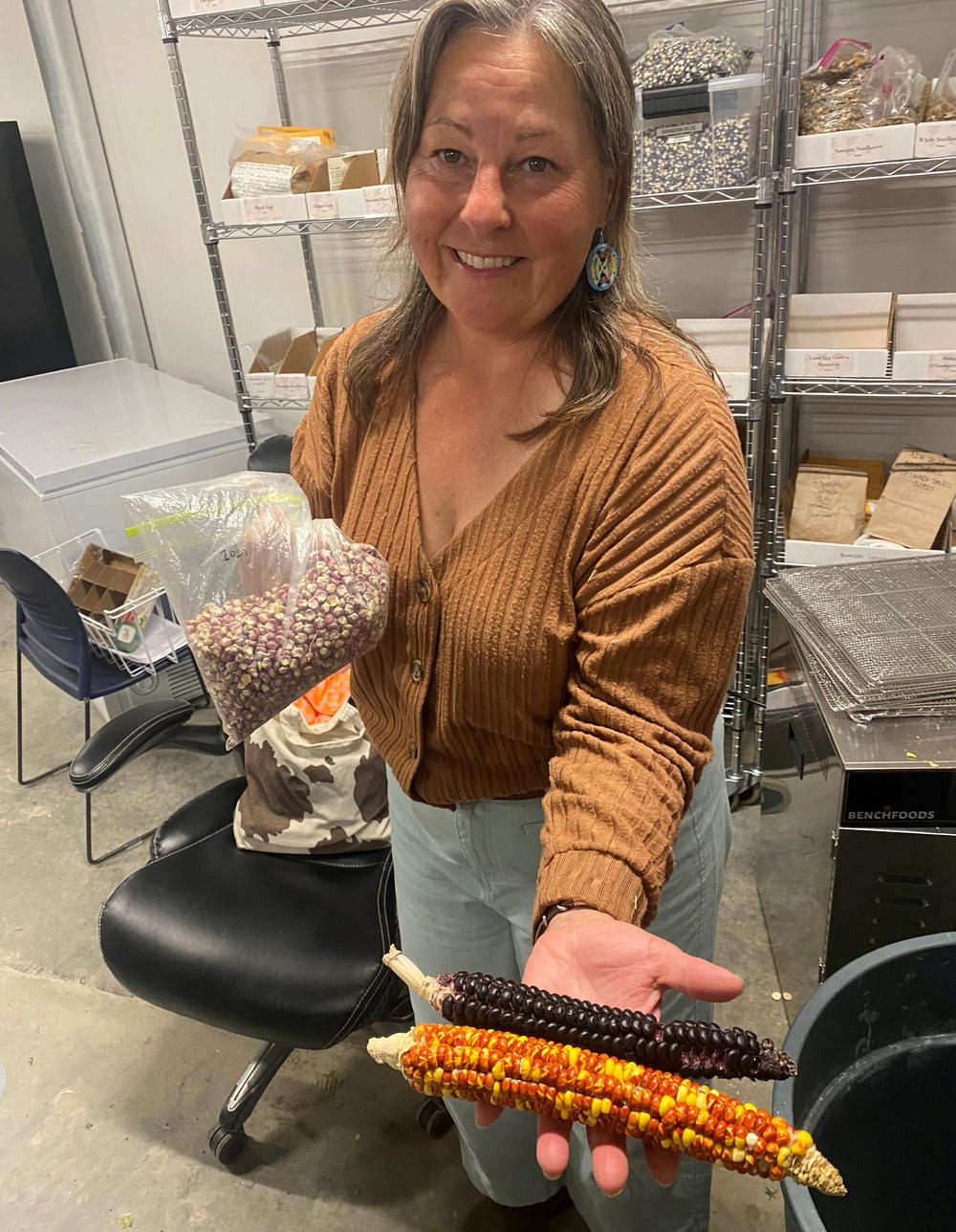 Jill Falcon Ramaker, director of the Buffalo Nations Food Systems Initiative at Montana State University, holds corn grown from the seed of ancient varieties once raised by the Mandan, Hidatsa, and Arikara peoples along the Missouri River in North Dakota. With her right hand, she holds a bag of Mandan Red Clay corn. In her left is an ear each of Mandan Society and Hopi Black corn varieties.