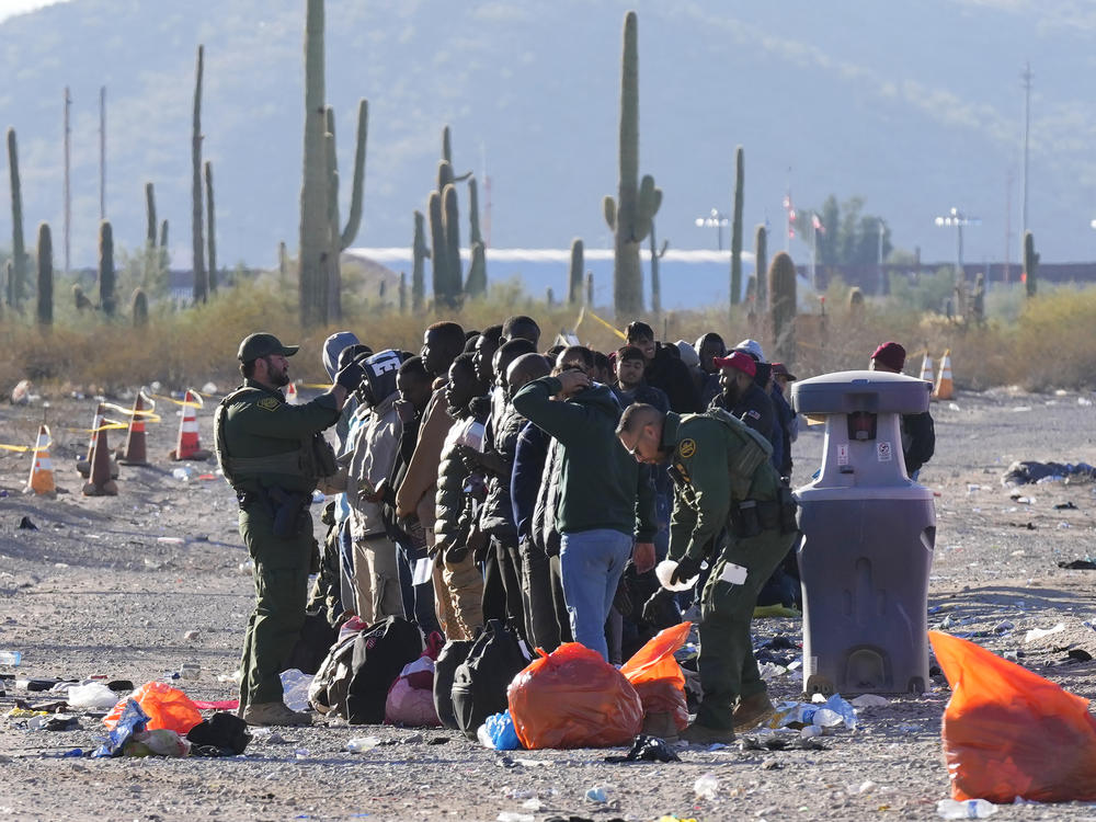 Members of the U.S. Border Patrol and U.S. Customs and Border Protection organize a group of migrants as hundreds of migrants gather along the border Tuesday, Dec. 5, 2023, in Lukeville, Ariz.