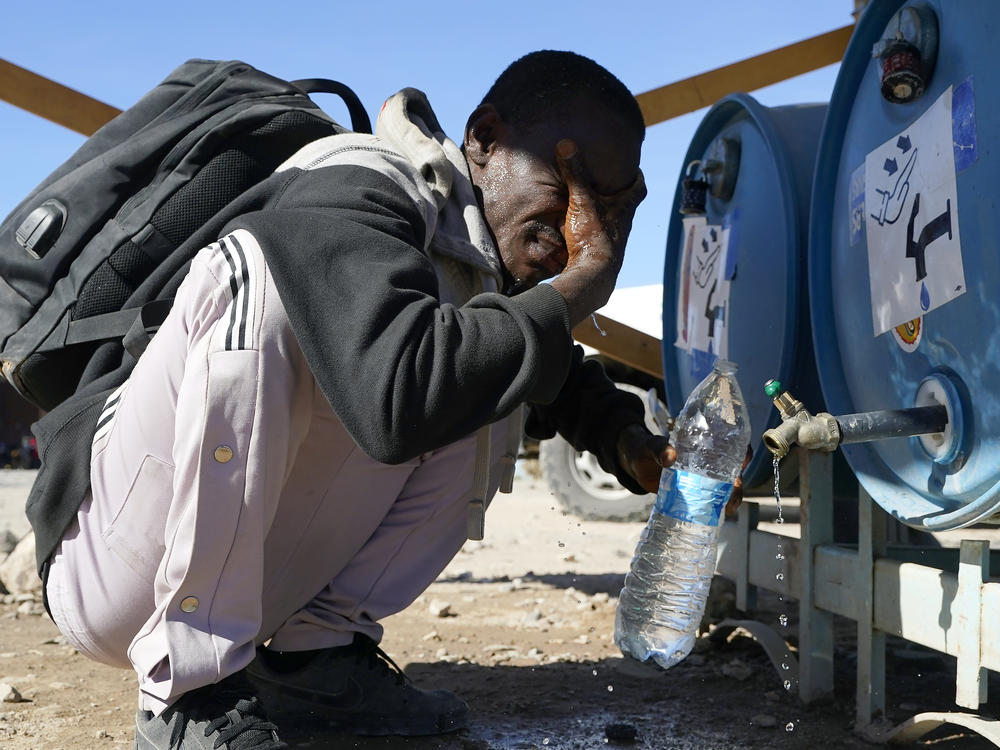A man from Kenya washes his face and fill his water bottle as hundreds of migrants gather along the border Tuesday, Dec. 5, 2023, in Lukeville, Ariz.