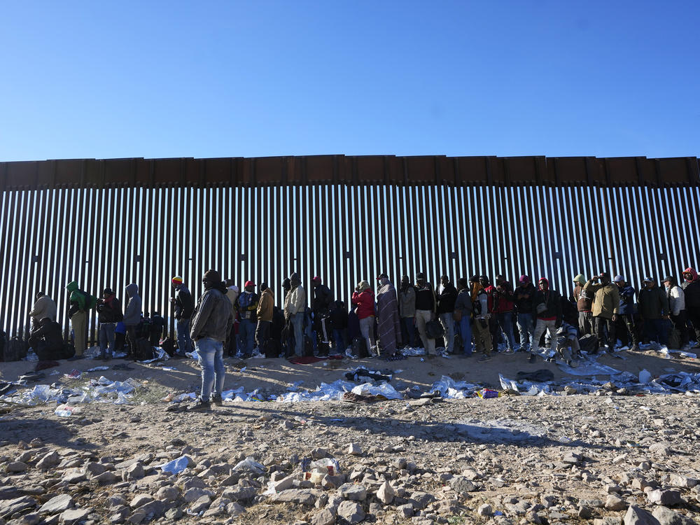 Hundreds of migrants gather along the border wall Tuesday, Dec. 5, 2023, in Lukeville, Ariz. The U.S. Border Patrol says it is overwhelmed by a shift in human smuggling routes.