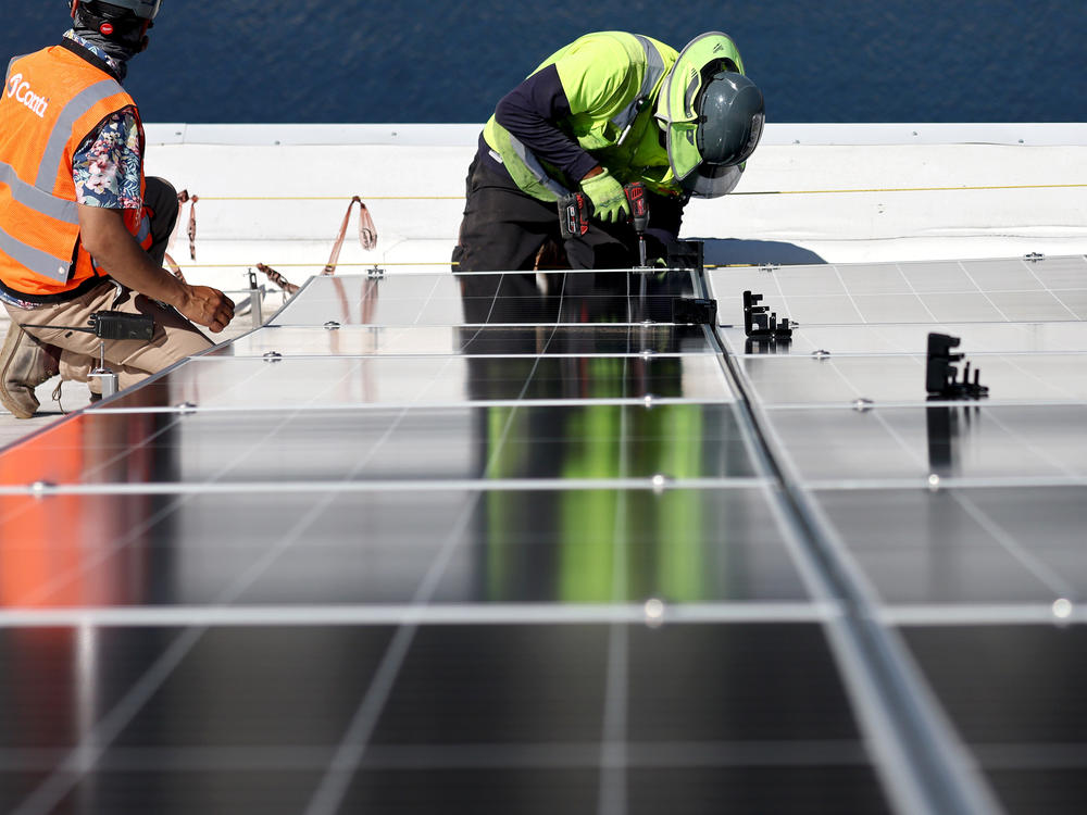 Workers install solar panels at the Port of Los Angeles on April 21. Although investing in renewables is still profitable, the returns currently aren't as high when compared with oil.