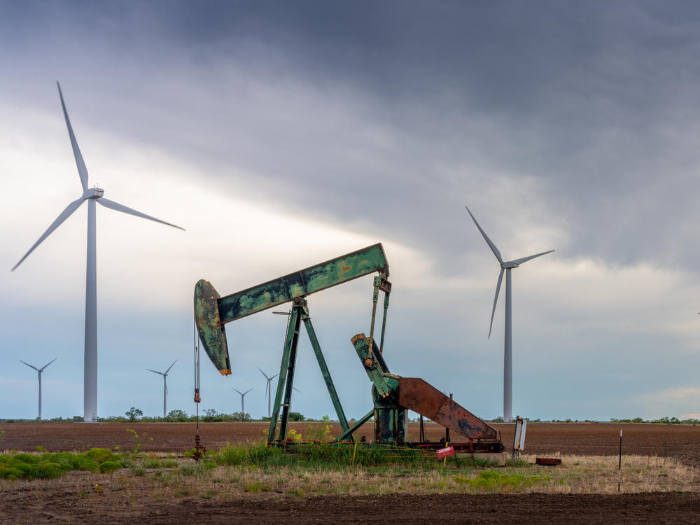 An oil pump jack stands near a field of wind turbines in Nolan, Texas, on Oct. 4. Oil companies are under pressure to pivot more swiftly toward renewable energy. Here's one reason why that's not happening so quickly: It's still incredibly lucrative to sell oil.
