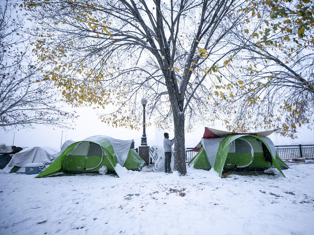 A man secures a tent in an encampment on Denver's Zuni Street, where migrants who had stayed in a city-contracted motel relocated after they had to leave the facility. Oct. 28, 2023.