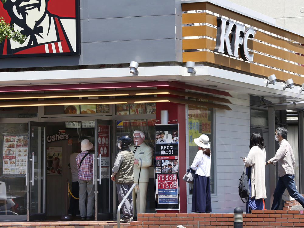 People wearing face masks to protect against the spread of the new coronavirus keep social distancing as they wait to enter a KFC restaurant in Yokohama near Tokyo on May 14, 2020.