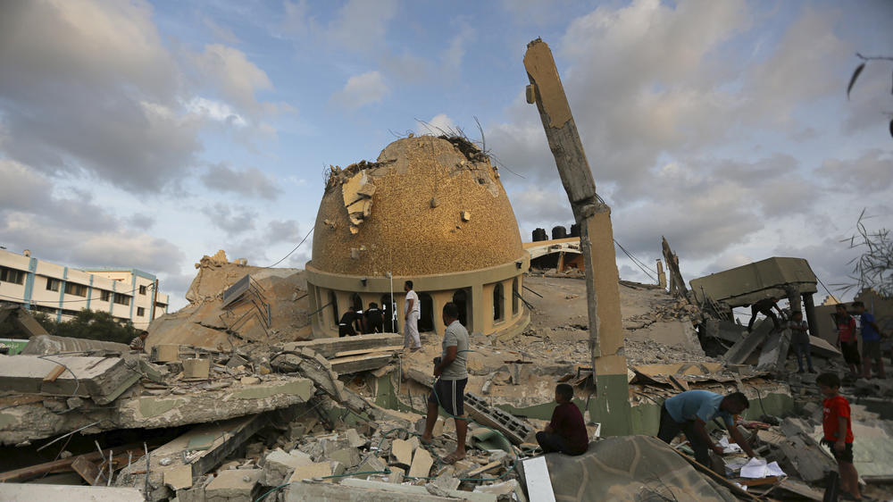 People stand outside a mosque destroyed in an Israeli air strike in Khan Younis, Gaza Strip, Sunday, Oct.8, 2023. The Hamas militants broke out of the blockaded Gaza Strip and rampaged through nearby Israeli communities, taking captives, while Israel's retaliation strikes leveled buildings in Gaza. (AP Photo/Yousef Masoud)