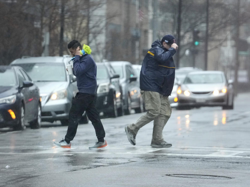 Pedestrians are buffeted by wind as they cross a street Monday in Boston.