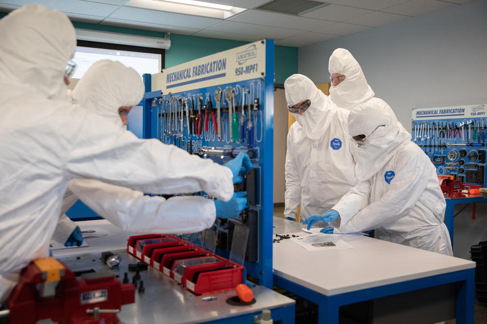 Students work in teams, handling washers, wrenches and bolts while dressed in the kind of gear worn inside clean rooms in semiconductor plants.