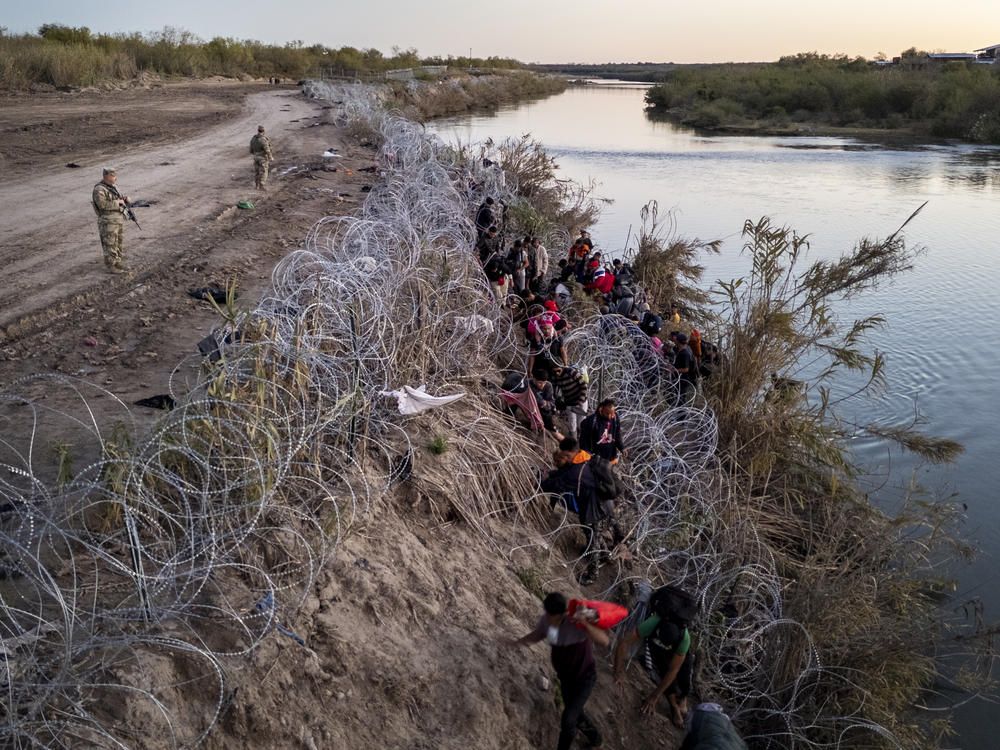 A Texas National guardsman watches as migrants pick their way through razor wire after crossing the Rio Grande into the United States on December 17, 2023 in Eagle Pass, Texas.