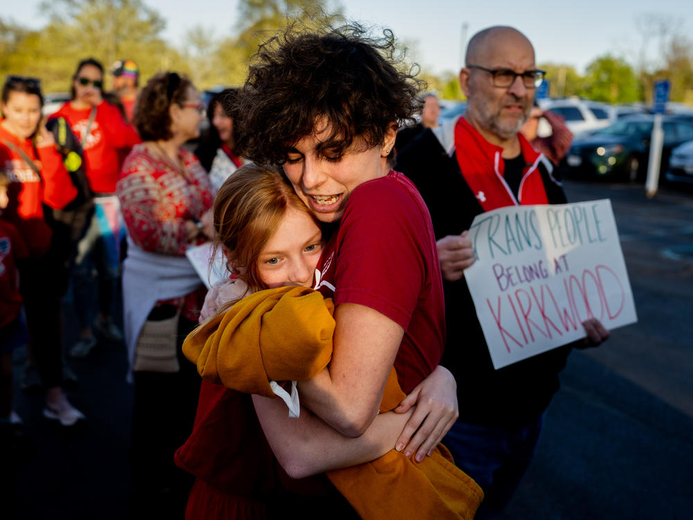 Hollis Moore, a 30-year-old teacher in the Kirkwood School District in Kirkwood, Mo., hugs their student Maggie McCoy, 10, on April 17, 2023, before a school board meeting outside the North Kirkwood Middle School. Moore alleges they have been discriminated against by district officials due to their gender identity. Full story <a href=