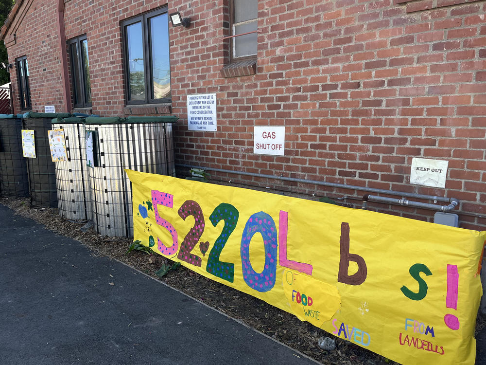 Kindergarten through eighth grade students at The Wesley School celebrate the harvest of the school's first compost with a banner marking how much food waste has been diverted from landfill.