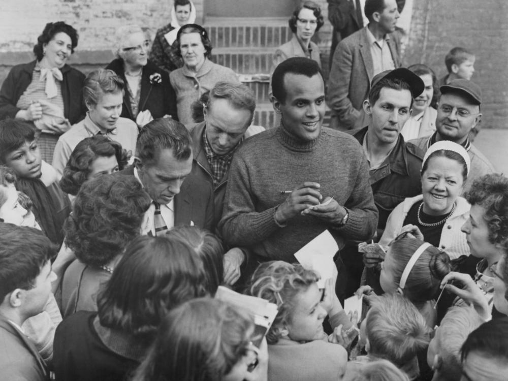 Harry Belafonte, alongside Ed Sullivan, signs autographs for fans outside CBS Studio 50 in New York City, circa 1955.