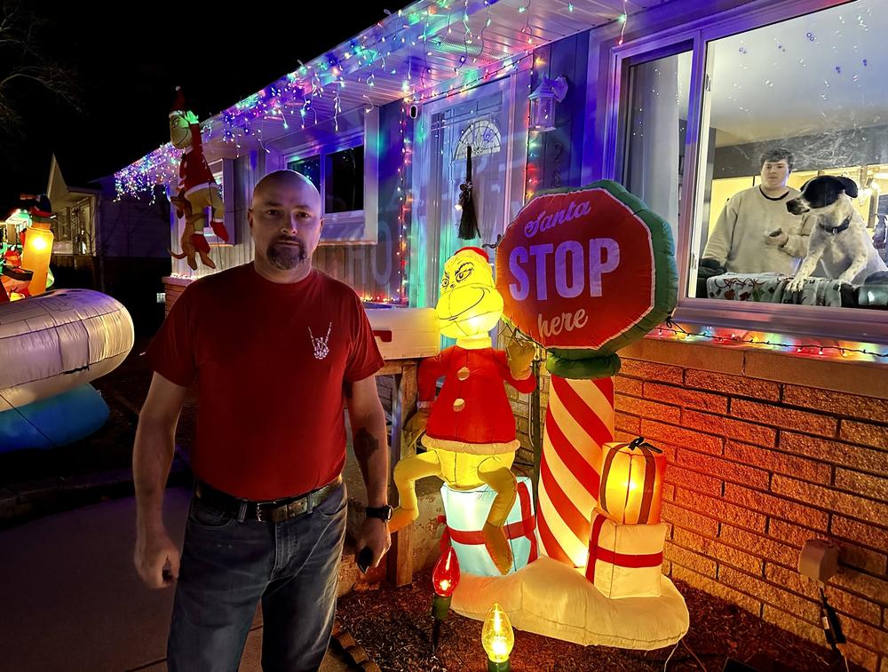 Mike Molloy poses near Grinch-themed decorations outside his home